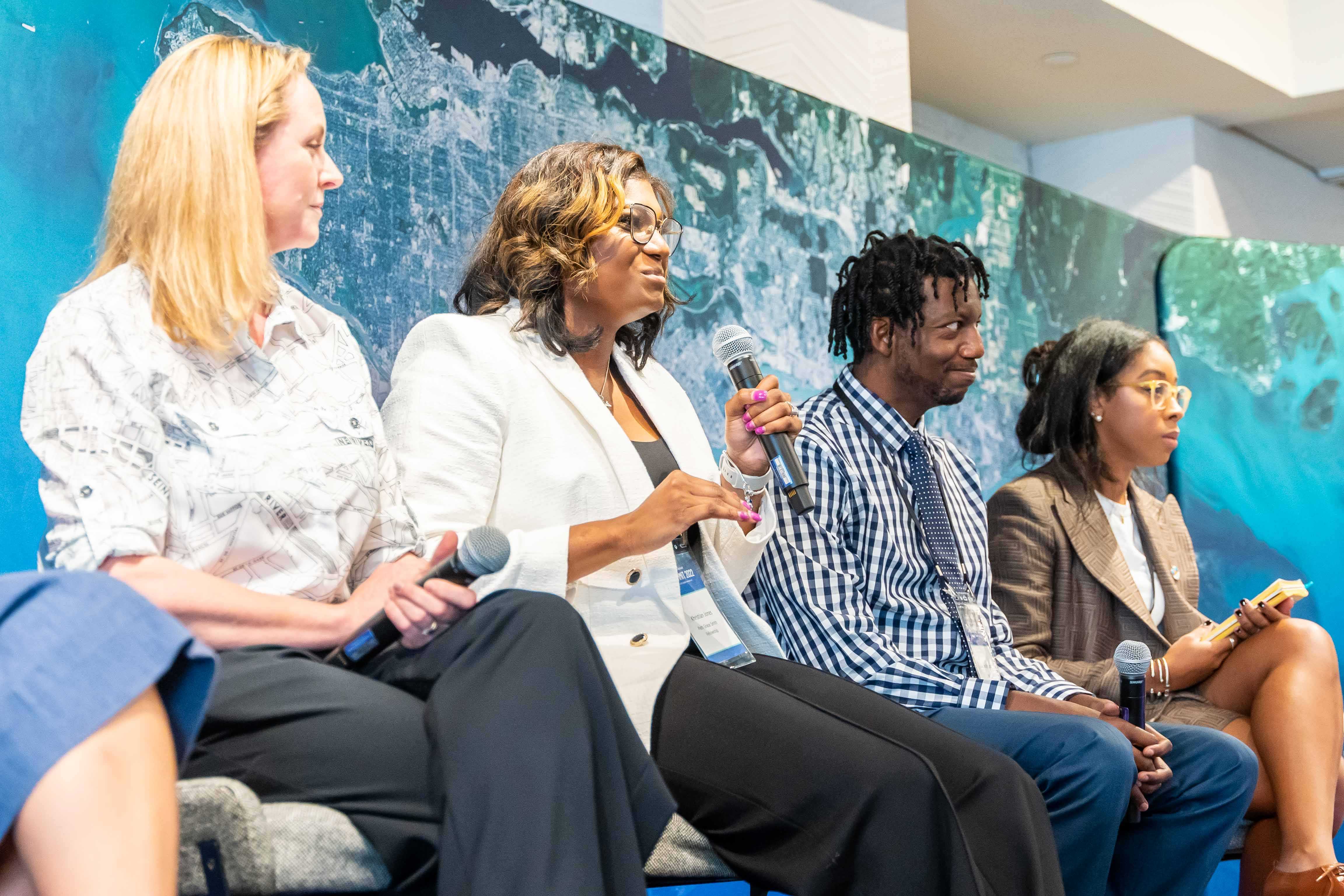 Four people sitting in line with the second one talking to a microphone